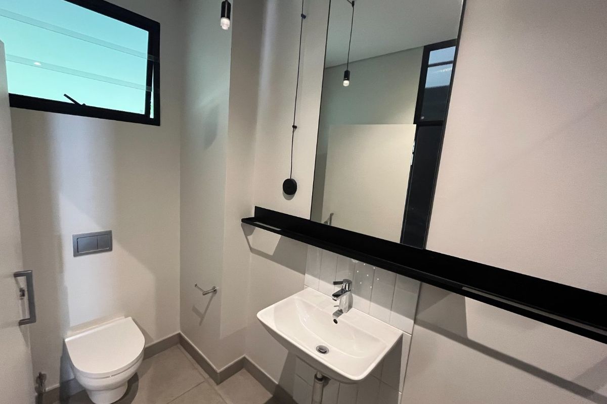 Modern guest bathroom featuring a wall-mounted toilet, sleek vanity basin, large mirror, and contemporary black fixtures.