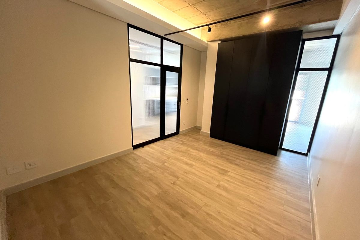 Modern bedroom featuring light wood-look flooring, exposed concrete ceiling, black built-in cabinetry, and industrial-style glass partition doors.