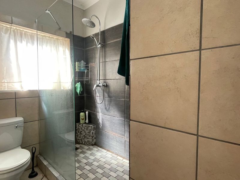 A functional bathroom featuring a walk-in shower with a glass screen, mosaic floor tiling, and neutral wall tiles.