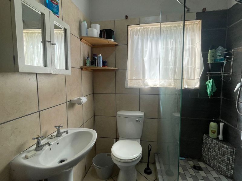 A functional bathroom featuring a pedestal basin, toilet, and a glass-enclosed shower with tiled finishes throughout.