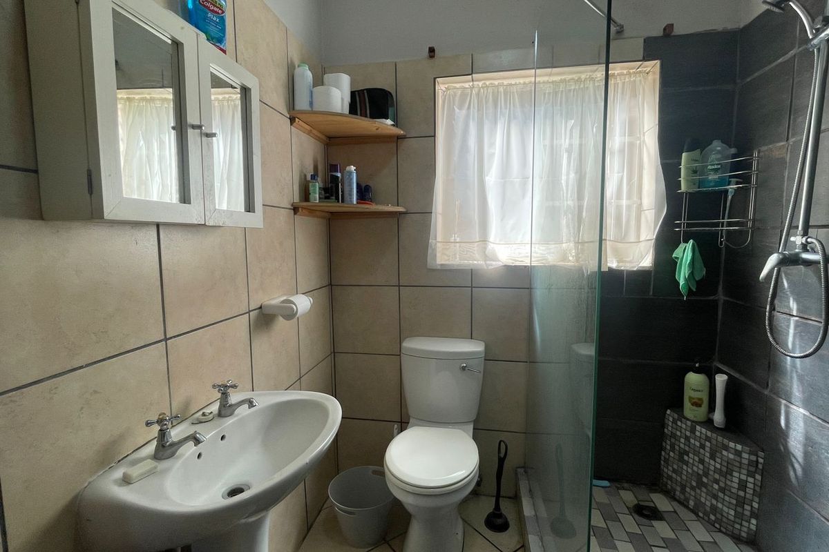 A functional bathroom featuring a pedestal basin, toilet, and a glass-enclosed shower with tiled finishes throughout.