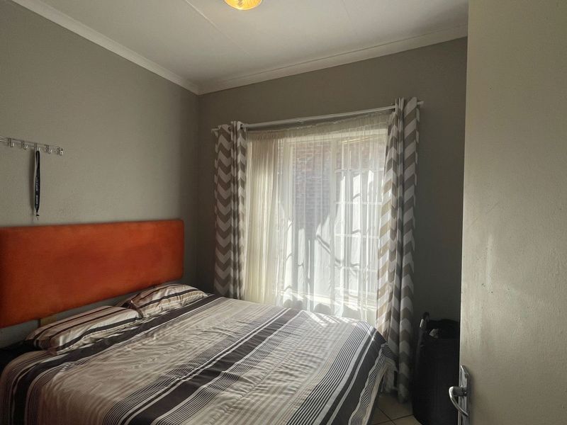 A functional bedroom featuring neutral wall tones, a window with curtain treatments, and standard ceiling lighting.