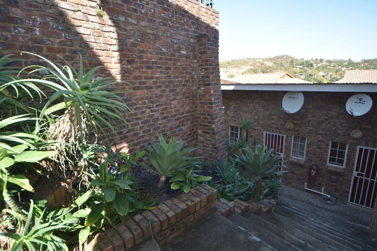 Exterior view of the apartment building featuring brick masonry, concrete stair access, and established garden beds with security gates.