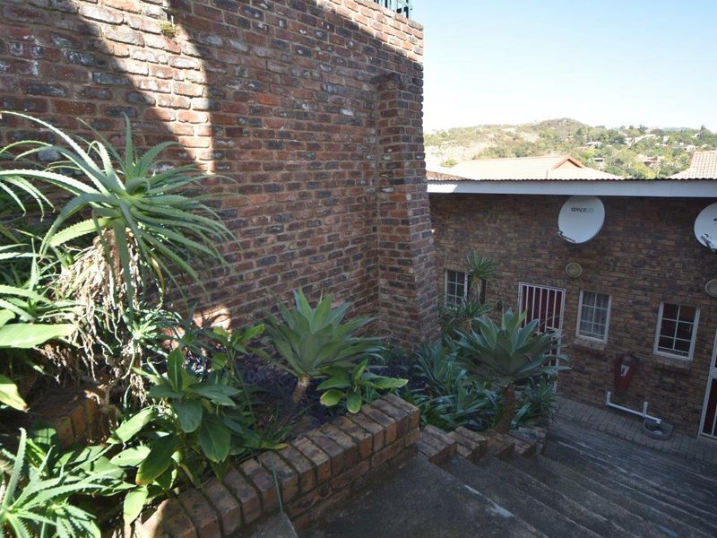 Exterior view of the apartment building featuring brick masonry, concrete stair access, and established garden beds with security gates.