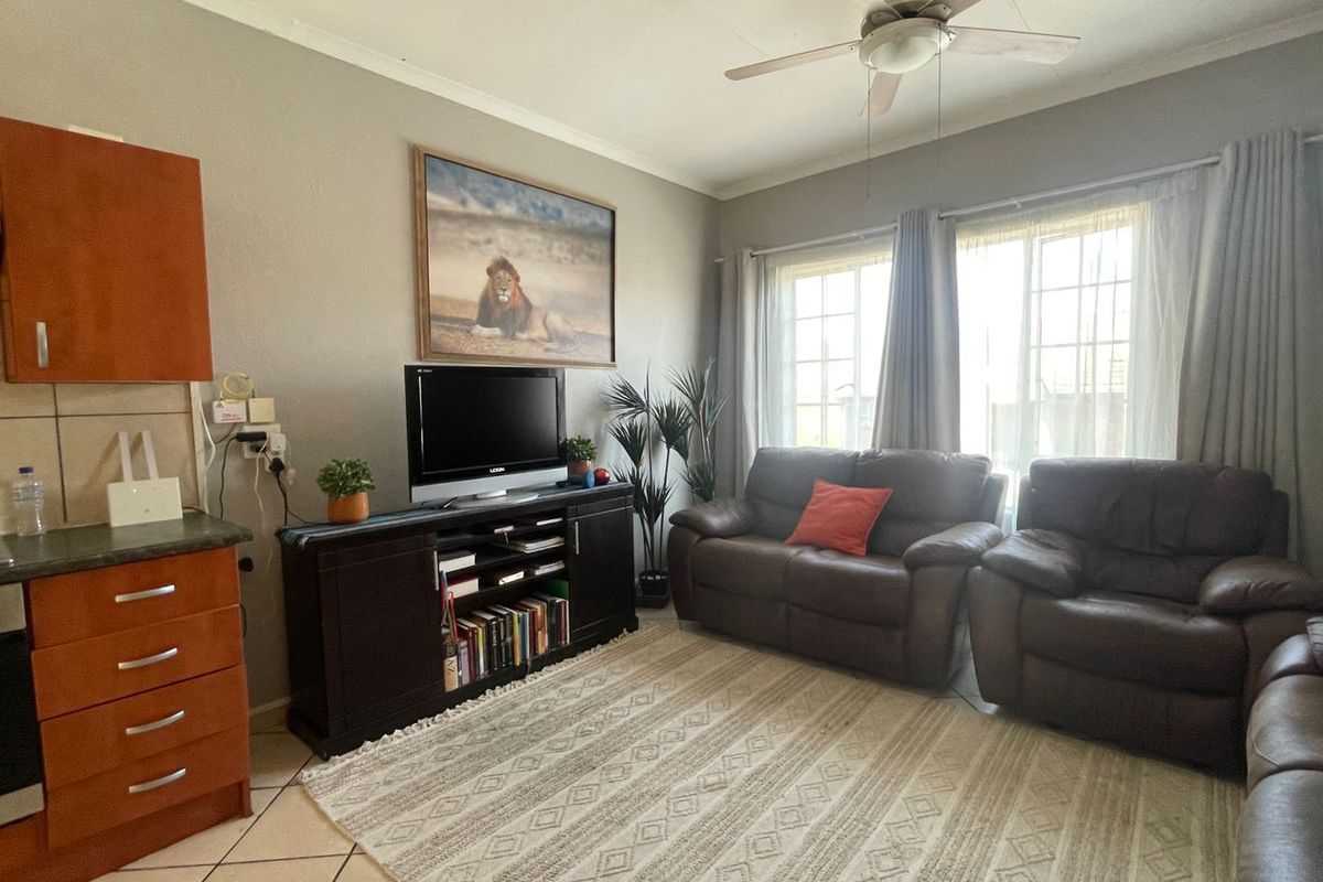 Open-plan living area featuring a compact kitchen with built-in cabinetry, gas hob, and oven, flowing into a comfortable lounge space with natural light.