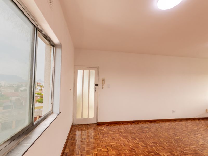 An empty living room featuring original parquet flooring, a large sliding window with neighborhood views, and a wall-mounted intercom system.