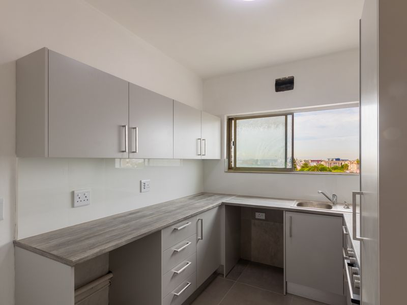 A clean, modern kitchen featuring light grey cabinetry, wood-look laminate countertops, a stainless steel sink, and tiled flooring with a view through the window.