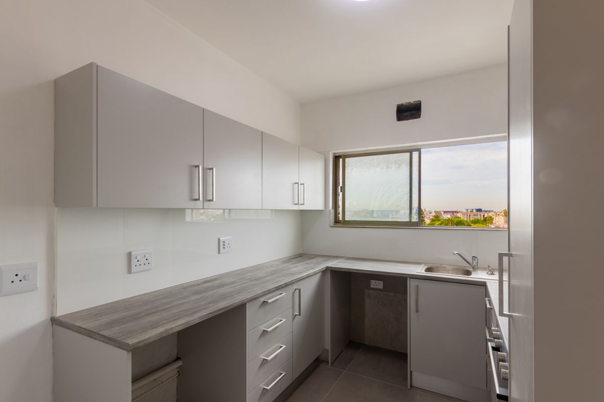 A clean, modern kitchen featuring light grey cabinetry, wood-look laminate countertops, a stainless steel sink, and tiled flooring with a view through the window.