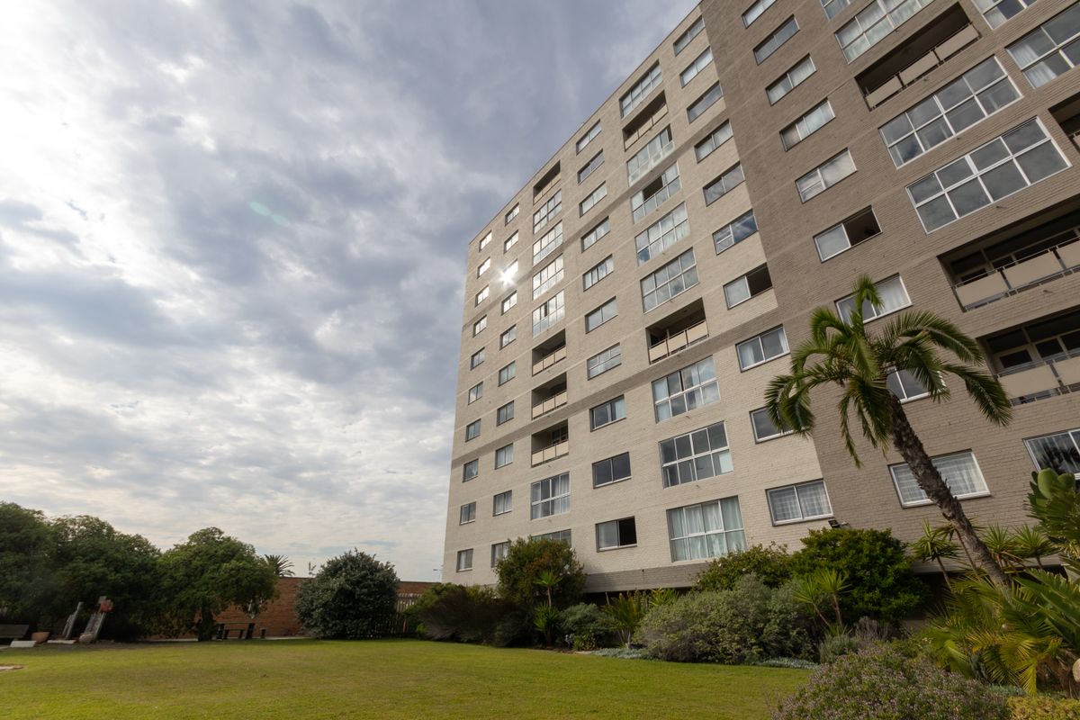 A low-angle view of a multi-story apartment building facade featuring balconies and an adjacent landscaped garden area.