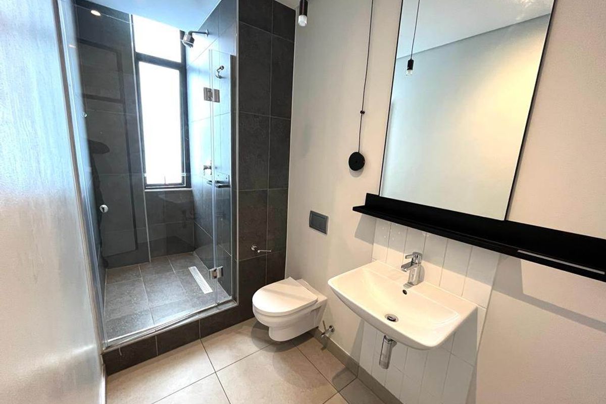 Modern bathroom featuring a glass-enclosed walk-in shower, wall-mounted toilet, and a sleek wall-hung basin with a large mirror.