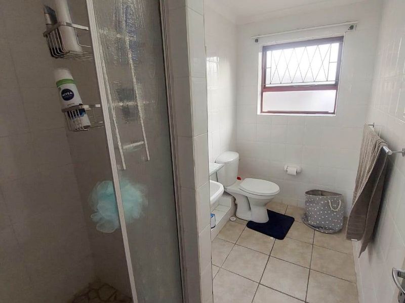 A functional bathroom featuring a shower enclosure, toilet, and washbasin with tiled finishes and a window providing natural light.