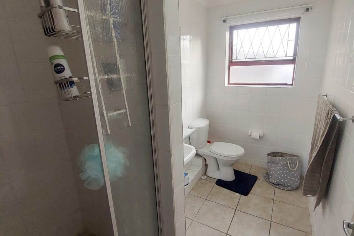 A functional bathroom featuring a shower enclosure, toilet, and washbasin with tiled finishes and a window providing natural light.