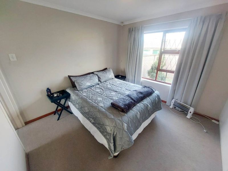 A functional bedroom featuring neutral carpet flooring, cove cornicing, and a window fitted with security burglar bars.