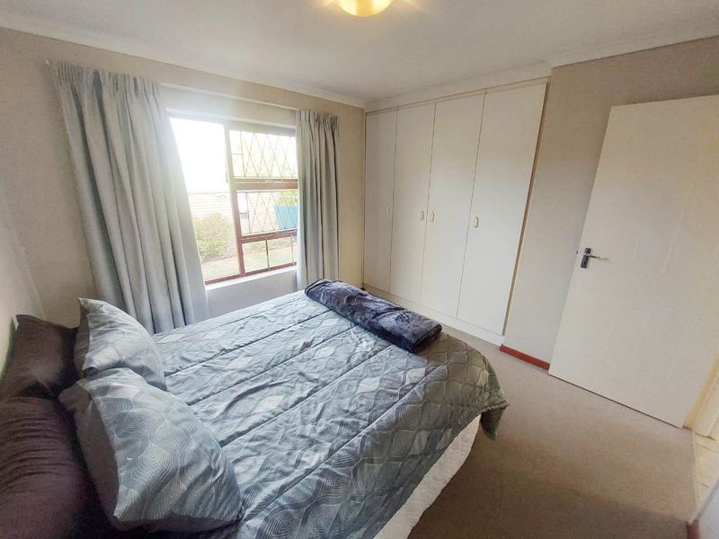 A functional bedroom featuring built-in cupboards, carpeted flooring, and a window with security burglar bars.