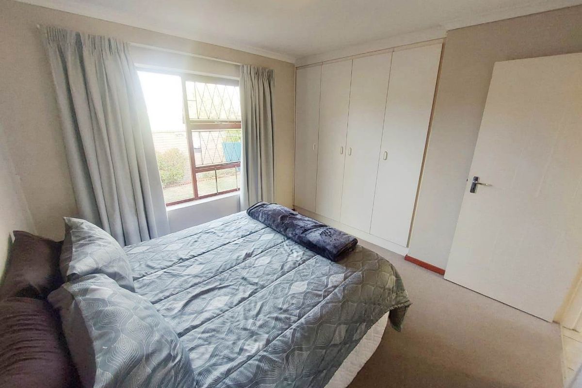 A functional bedroom featuring built-in cupboards, carpeted flooring, and a window with security burglar bars.