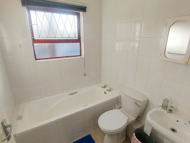 A functional bathroom featuring a bathtub, pedestal sink, and toilet with white wall tiling and tiled flooring.