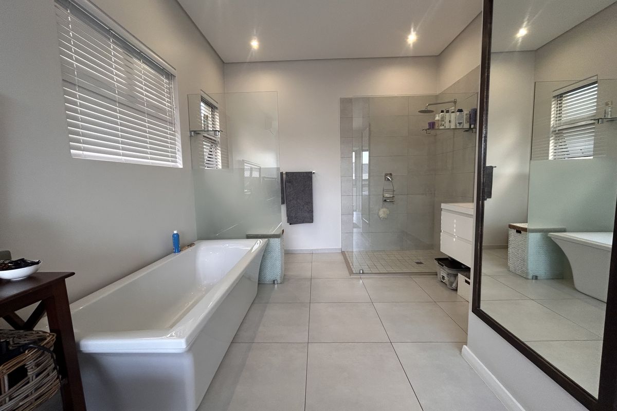 Modern bathroom featuring a freestanding bathtub, a spacious walk-in shower with glass enclosure, vanity cabinet, and large wall mirror with neutral floor tiling.