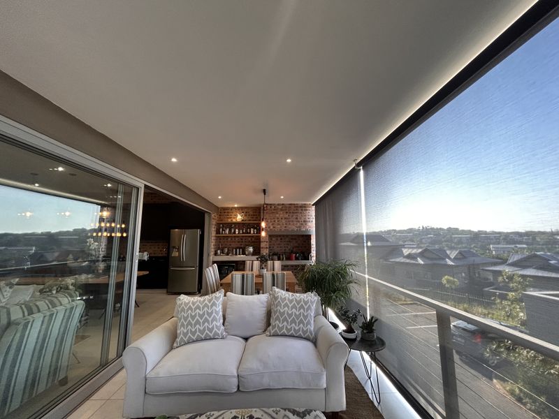 Spacious covered balcony featuring a built-in braai, exposed brick accents, recessed lighting, and retractable sun screens, offering an ideal space for outdoor entertaining.