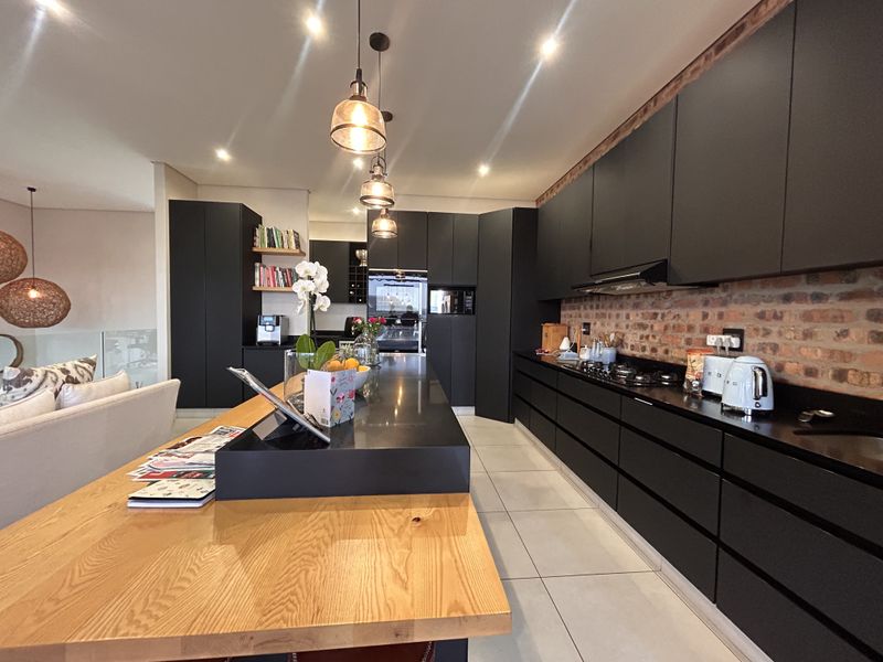 Modern kitchen featuring matte black cabinetry, a large island with a wooden breakfast bar, exposed brick backsplash, and high-end integrated appliances.