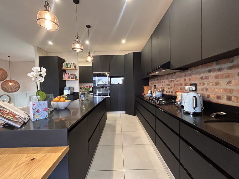 Modern kitchen featuring sleek black cabinetry, stone countertops, an exposed brick backsplash, and high-end built-in appliances with stylish pendant lighting.