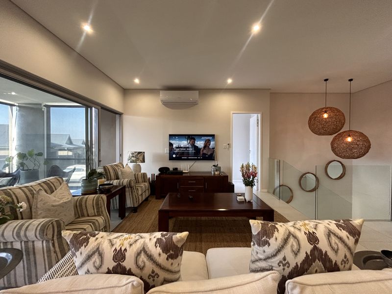 A well-lit living room featuring recessed downlights, a split-system air conditioner, and a modern glass balustrade overlooking the staircase.