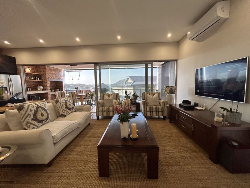 Spacious open-plan living area featuring recessed lighting, air conditioning, and seamless flow to a covered patio with a built-in braai and scenic views.