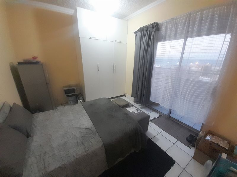 A bedroom featuring built-in wardrobes, tiled flooring, and a sliding glass door providing access to an outdoor balcony area.