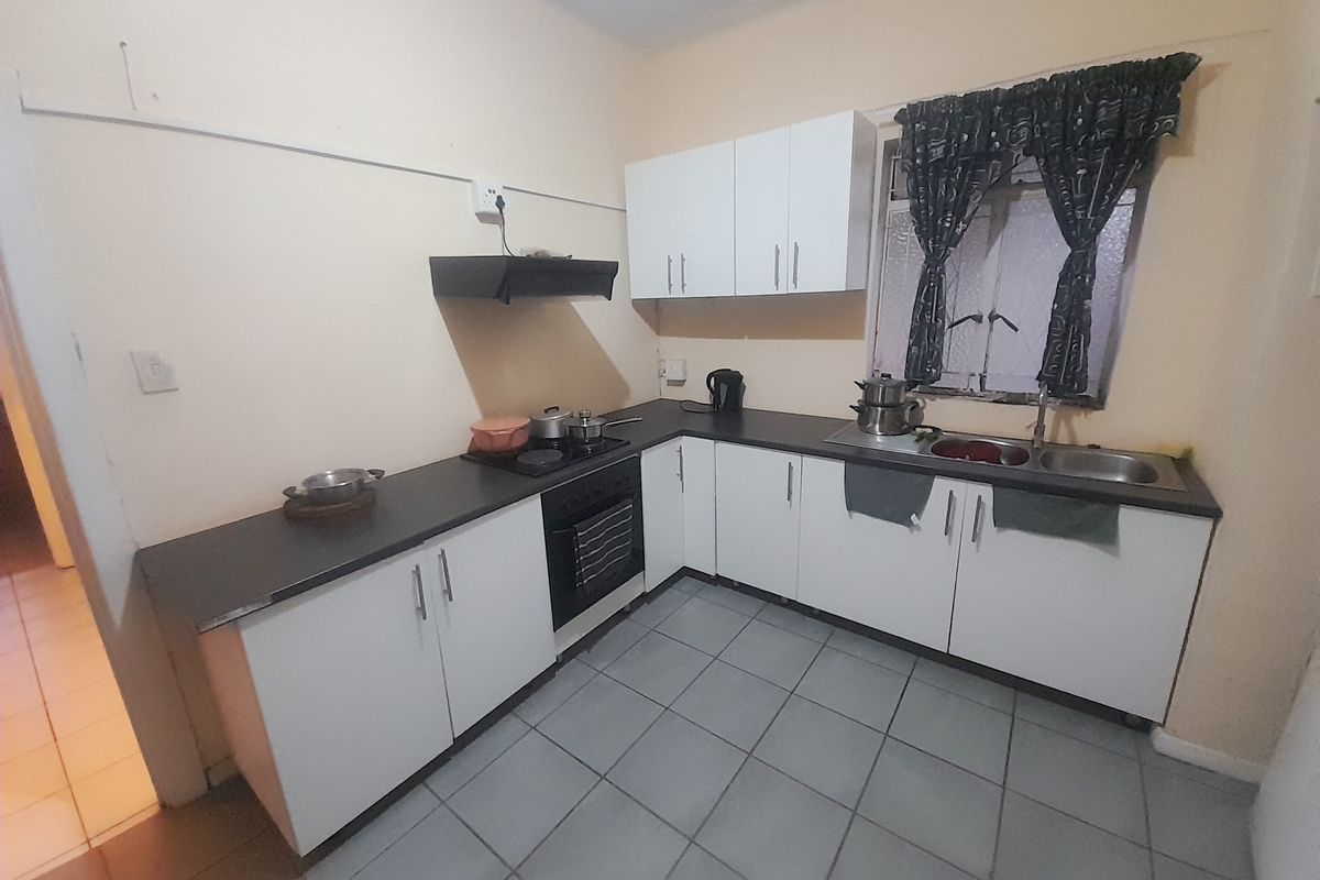 A functional kitchen featuring white cabinetry, dark laminate countertops, a built-in oven with hob, and tiled flooring.