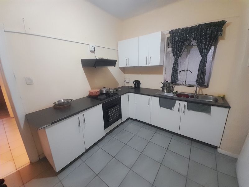 A functional kitchen featuring white cabinetry, dark laminate countertops, a built-in oven with hob, and tiled flooring.