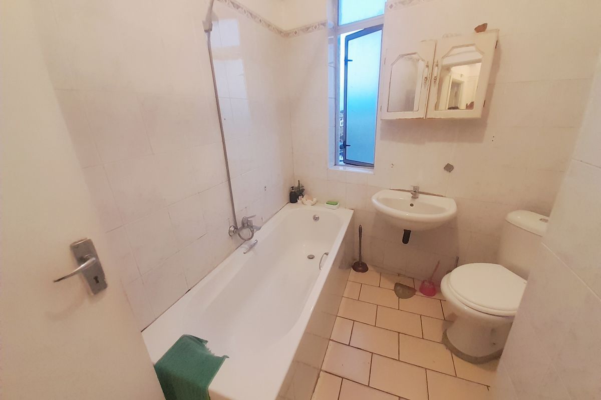 A dated bathroom featuring a bathtub with shower attachment, pedestal basin, toilet, and wall-mounted medicine cabinet, finished with tiled walls and flooring.