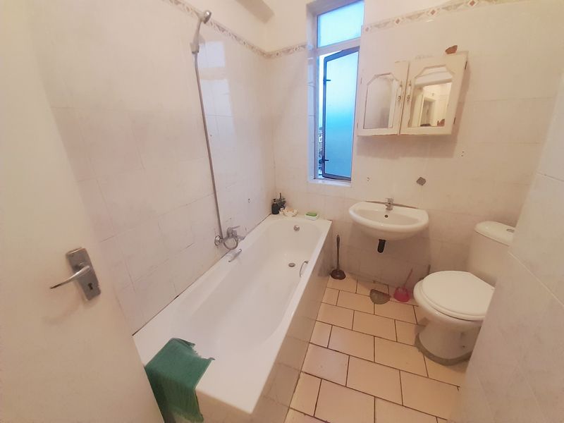 A dated bathroom featuring a bathtub with shower attachment, pedestal basin, toilet, and wall-mounted medicine cabinet, finished with tiled walls and flooring.