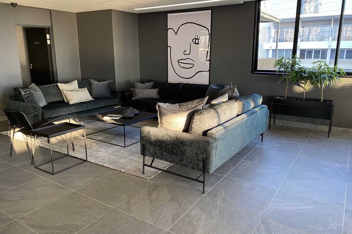 A modern, well-lit living area featuring large format floor tiles, dark feature walls, and expansive windows providing ample natural light.