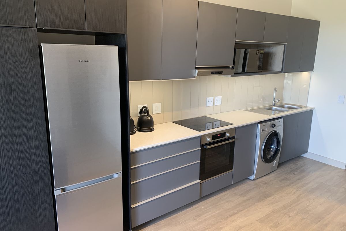 Modern kitchen featuring sleek grey cabinetry, stone countertops, integrated appliances, and a tiled splashback, offering a clean and functional culinary space.