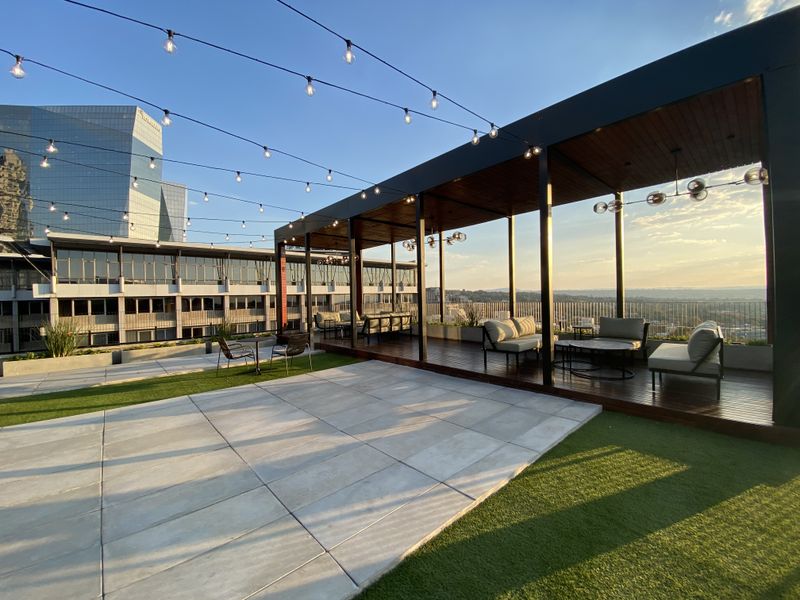 Spacious rooftop terrace featuring a timber-decked pergola, integrated string lighting, paved areas, and artificial turf with expansive city views.