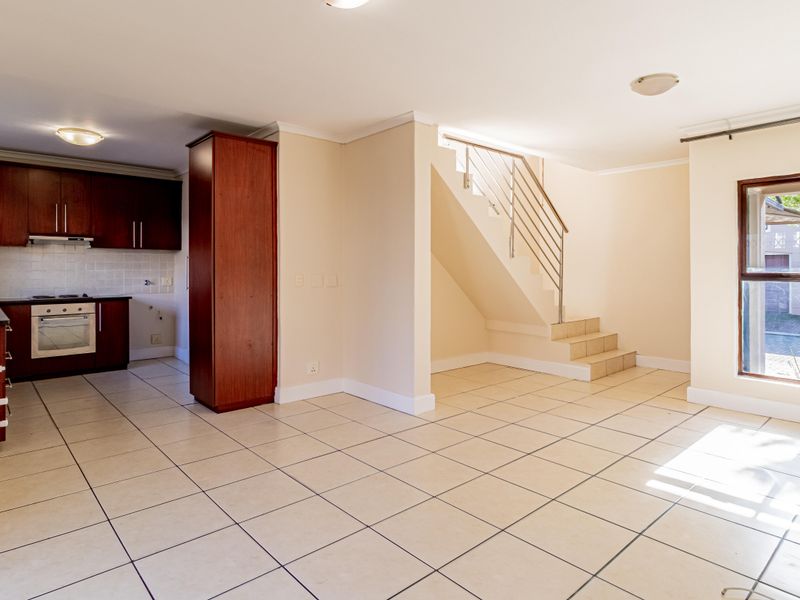 Open-plan living area featuring tiled floors, a functional kitchen with built-in appliances, and a staircase with a metal balustrade.