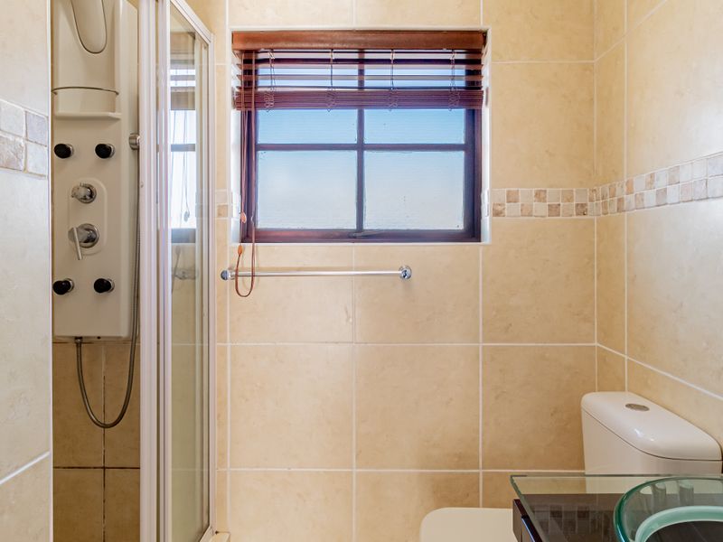 A functional bathroom featuring a shower cubicle with a massage panel, a glass vessel sink, and neutral wall tiling.
