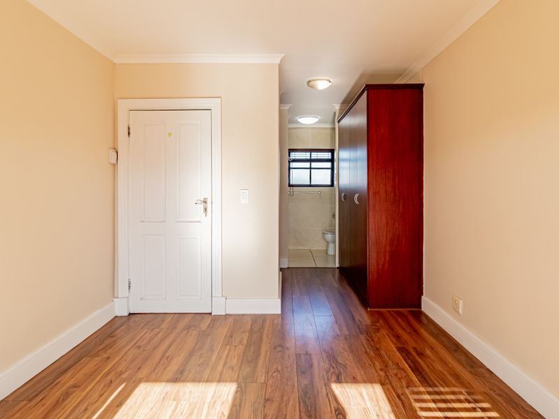 A bright, empty bedroom featuring laminate flooring, coving, and a built-in cupboard, with an adjoining en-suite bathroom visible through the doorway.