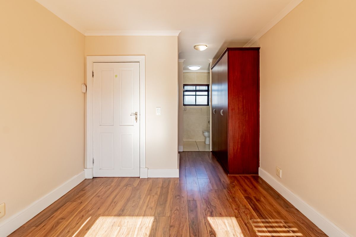 A bright, empty bedroom featuring laminate flooring, coving, and a built-in cupboard, with an adjoining en-suite bathroom visible through the doorway.