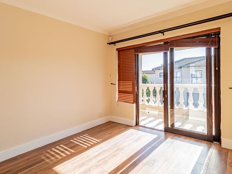 A bright, empty bedroom featuring laminate flooring and a sliding glass door that opens onto a private balcony.