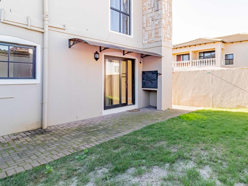 Rear exterior view of the townhouse featuring a paved patio area, built-in braai, and a private garden with a boundary wall.