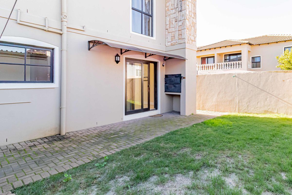 Rear exterior view of the townhouse featuring a paved patio area, built-in braai, and a private garden with a boundary wall.