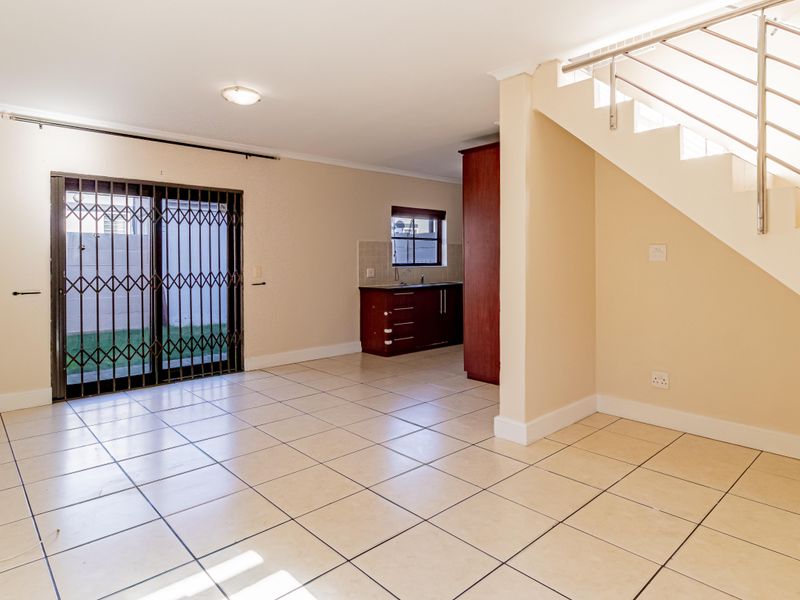 Open-plan living area featuring tiled flooring, a staircase with a metal balustrade, and direct access to the rear garden through a sliding glass door.