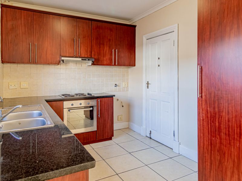 A functional kitchen featuring dark wood cabinetry, granite countertops, a built-in oven, electric hob, and tiled flooring.