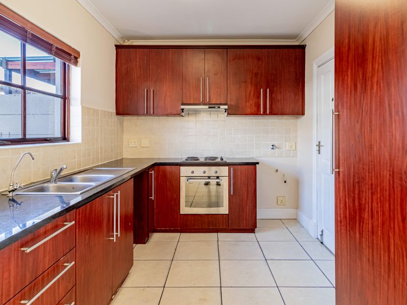 A functional kitchen featuring dark wood cabinetry, laminate countertops, built-in oven, hob, extractor fan, and tiled flooring.