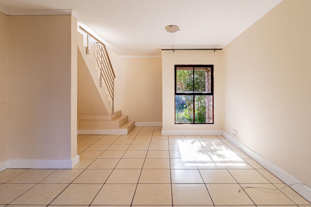 An empty, light-filled living area featuring neutral walls, tiled flooring, and a staircase with a modern metal balustrade.
