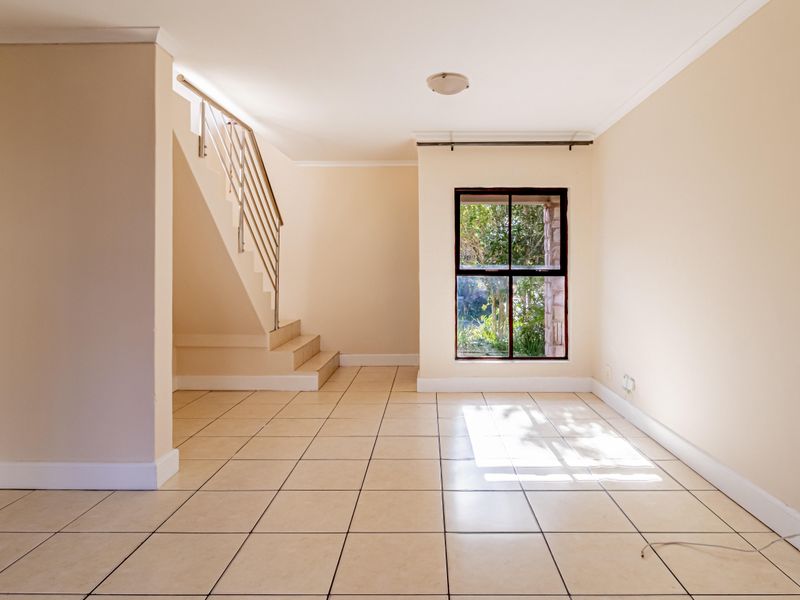 An empty, light-filled living area featuring neutral walls, tiled flooring, and a staircase with a modern metal balustrade.