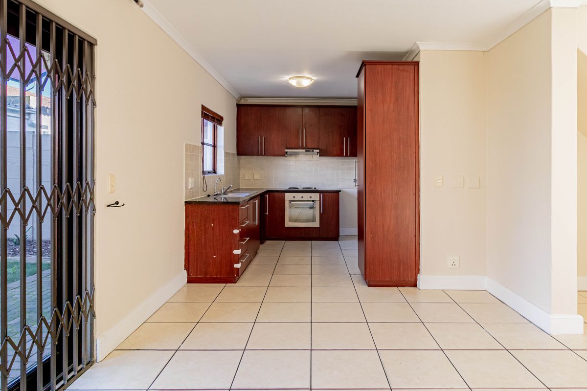 A functional kitchen featuring dark wood cabinetry, built-in oven and hob, tiled splashbacks, and direct access to the outdoor area via a security gate.
