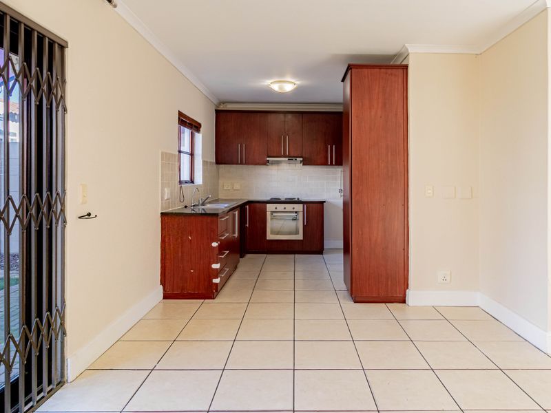 A functional kitchen featuring dark wood cabinetry, built-in oven and hob, tiled splashbacks, and direct access to the outdoor area via a security gate.