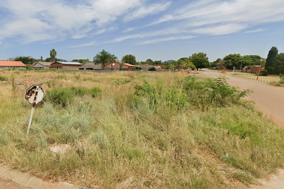 A street-level view of a vacant residential plot featuring overgrown grass and direct access to the adjacent paved road.