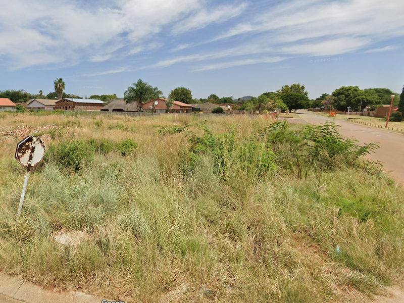 A street-level view of a vacant residential plot featuring overgrown grass and direct access to the adjacent paved road.